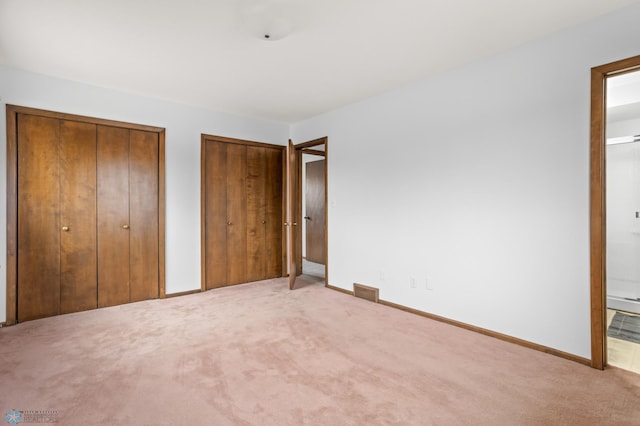 unfurnished bedroom with multiple closets and light carpet