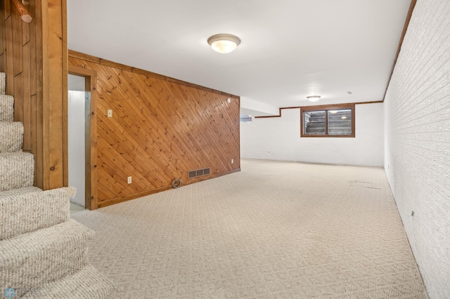 basement featuring ornamental molding, wooden walls, and carpet floors