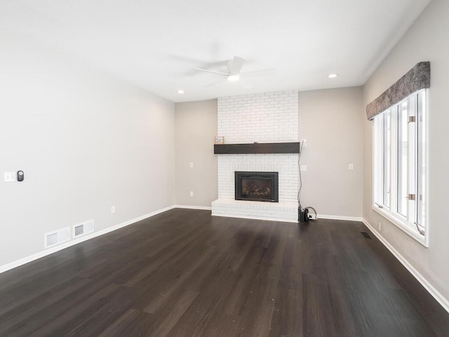 unfurnished living room with a brick fireplace, dark hardwood / wood-style floors, and ceiling fan