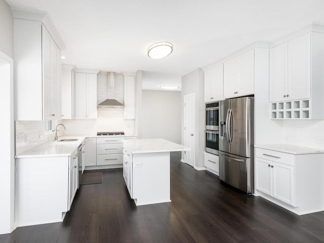 kitchen with white cabinetry, sink, a center island, stainless steel appliances, and wall chimney range hood