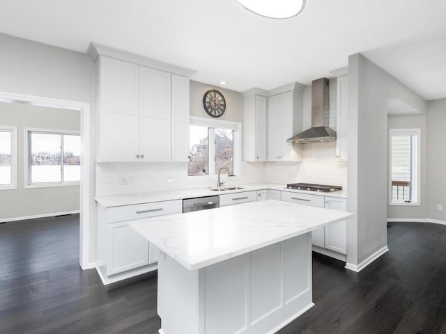 kitchen with wall chimney exhaust hood, sink, a kitchen island, light stone countertops, and white cabinets