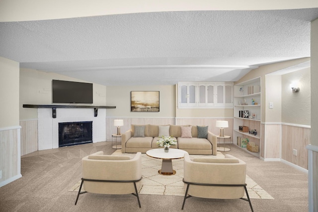 living room featuring built in shelves, vaulted ceiling, a textured ceiling, light colored carpet, and a fireplace