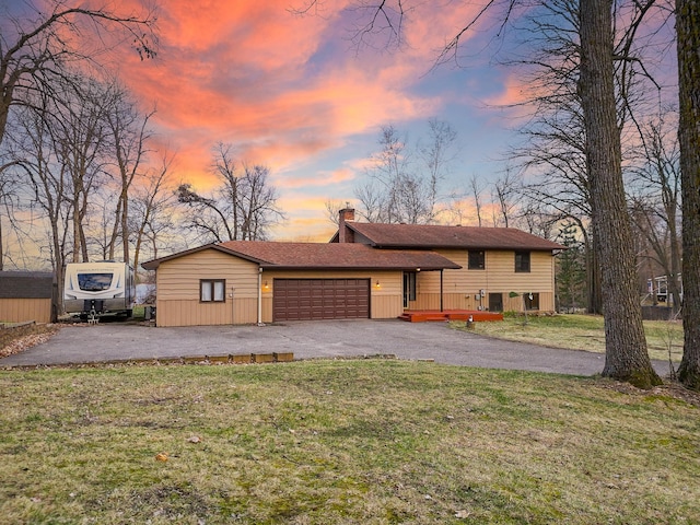 tri-level home featuring a front lawn, a chimney, aphalt driveway, and a garage