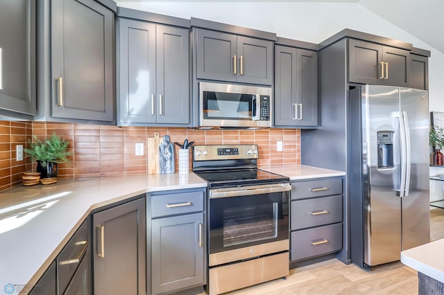 kitchen with gray cabinetry, vaulted ceiling, light hardwood / wood-style flooring, stainless steel appliances, and backsplash