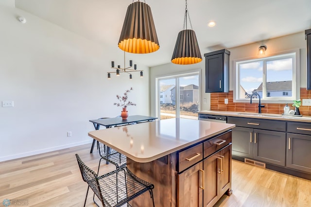 kitchen with a breakfast bar, sink, a center island, hanging light fixtures, and light wood-type flooring