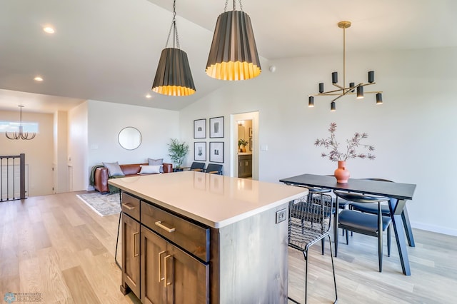 kitchen featuring vaulted ceiling, a kitchen island, hanging light fixtures, an inviting chandelier, and light hardwood / wood-style flooring