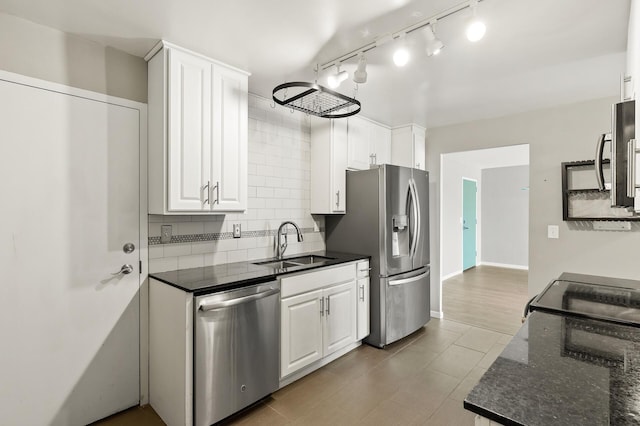 kitchen featuring appliances with stainless steel finishes, white cabinetry, sink, backsplash, and dark stone counters