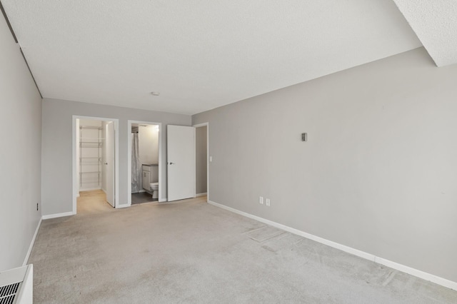 unfurnished bedroom featuring light carpet, a walk in closet, a textured ceiling, and ensuite bathroom