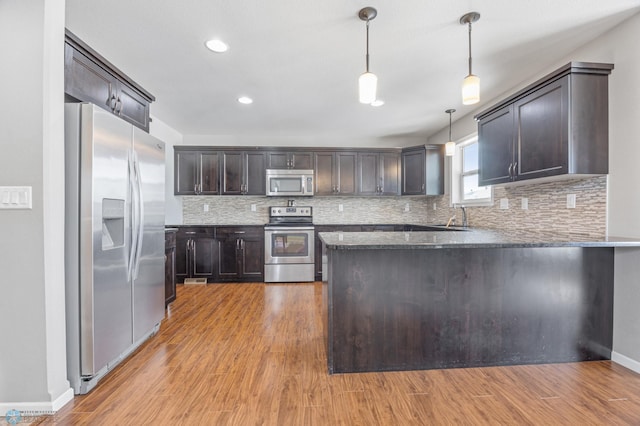 kitchen featuring pendant lighting, stainless steel appliances, kitchen peninsula, and light hardwood / wood-style floors