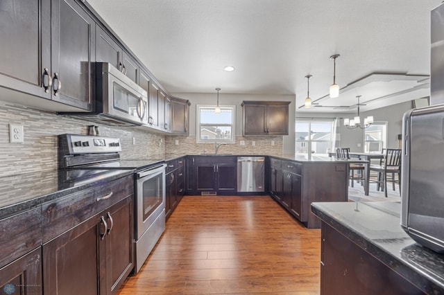 kitchen featuring dark brown cabinetry, hanging light fixtures, dark hardwood / wood-style floors, stainless steel appliances, and decorative backsplash