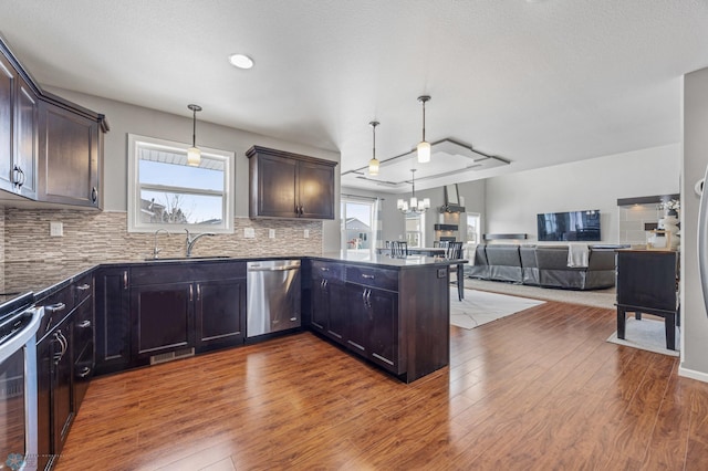 kitchen with appliances with stainless steel finishes, sink, decorative backsplash, hanging light fixtures, and kitchen peninsula