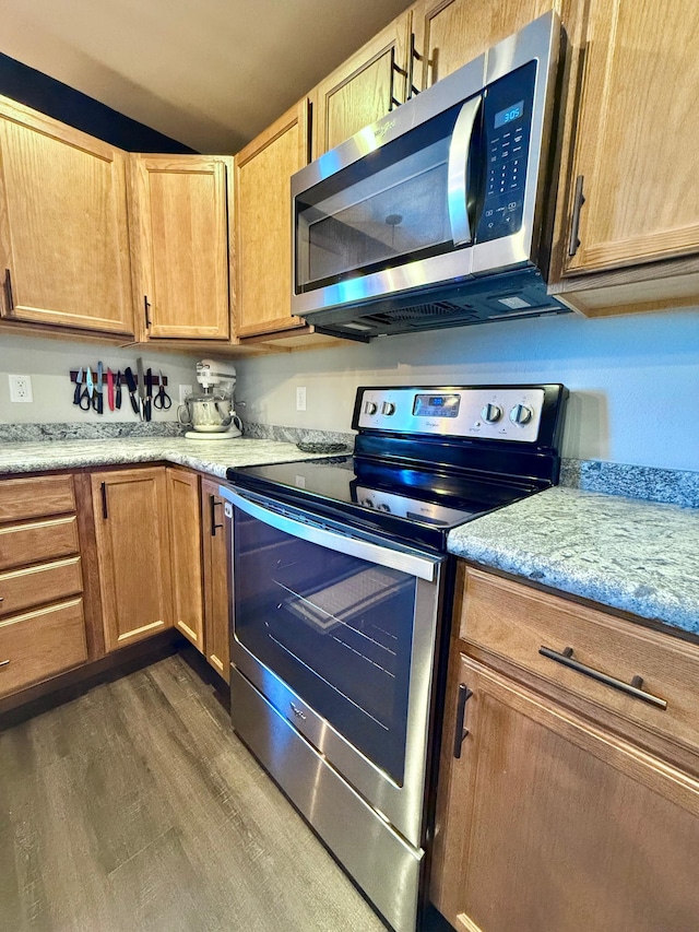 kitchen featuring stainless steel appliances, light stone countertops, and dark wood-type flooring