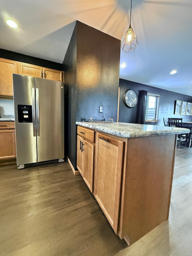 kitchen with dark wood-type flooring, pendant lighting, light stone counters, and stainless steel fridge with ice dispenser