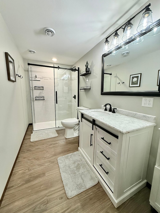 bathroom featuring hardwood / wood-style flooring, vanity, a shower with door, and toilet