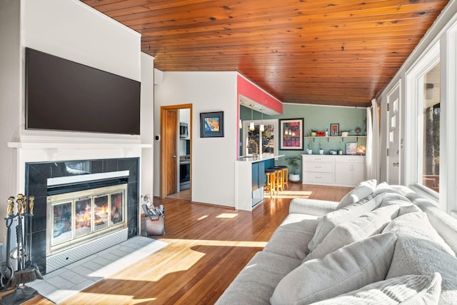 living room featuring a tile fireplace, vaulted ceiling, a healthy amount of sunlight, and light hardwood / wood-style floors