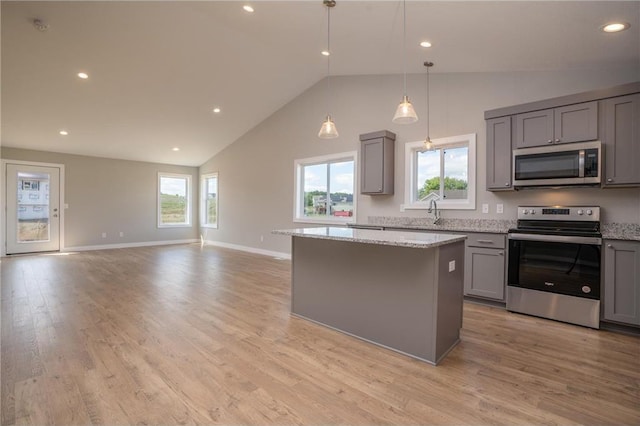 kitchen featuring a kitchen island, appliances with stainless steel finishes, gray cabinetry, light stone countertops, and light hardwood / wood-style flooring