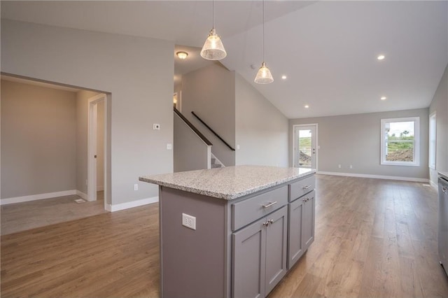 kitchen with light stone counters, light wood-type flooring, gray cabinets, a kitchen island, and pendant lighting