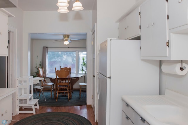 kitchen with dark hardwood / wood-style flooring, ceiling fan with notable chandelier, white fridge, and white cabinets