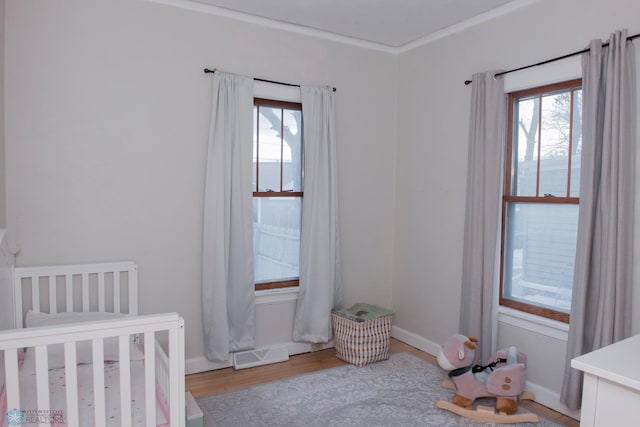 bedroom featuring a nursery area, ornamental molding, multiple windows, and light wood-type flooring