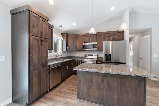 kitchen with sink, light stone counters, dark brown cabinets, appliances with stainless steel finishes, and a kitchen island