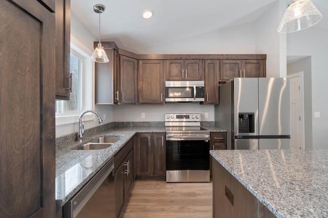 kitchen featuring lofted ceiling, sink, hanging light fixtures, appliances with stainless steel finishes, and light stone countertops