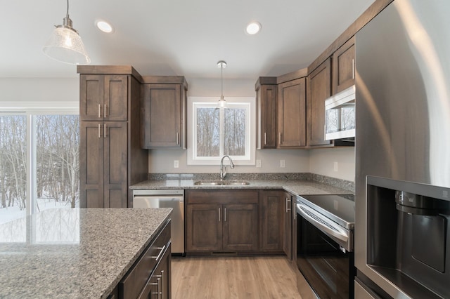 kitchen with sink, appliances with stainless steel finishes, light stone countertops, decorative light fixtures, and light wood-type flooring