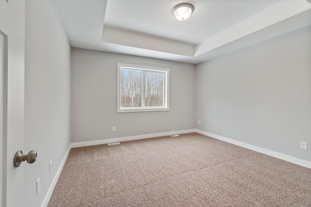 empty room with a raised ceiling and carpet flooring