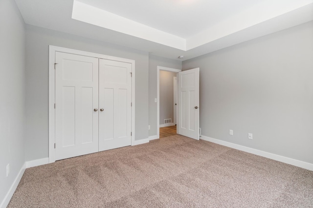 unfurnished bedroom with a closet, a tray ceiling, and carpet