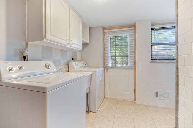 clothes washing area featuring washer and dryer, cabinets, a textured ceiling, and light tile patterned flooring