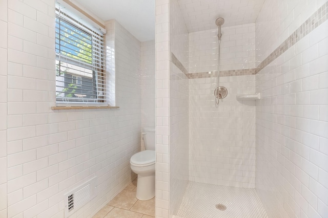 bathroom with tile walls, tile patterned floors, toilet, and tiled shower