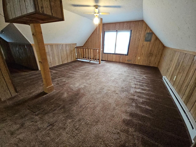 additional living space with dark colored carpet, vaulted ceiling, wooden walls, and baseboard heating