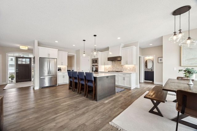 kitchen featuring white cabinetry, decorative backsplash, hanging light fixtures, stainless steel appliances, and a center island with sink