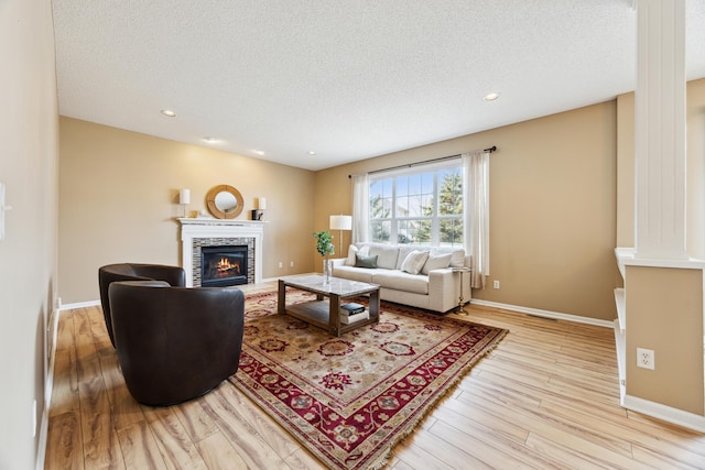 living room featuring a textured ceiling, a tile fireplace, light wood-style flooring, and baseboards