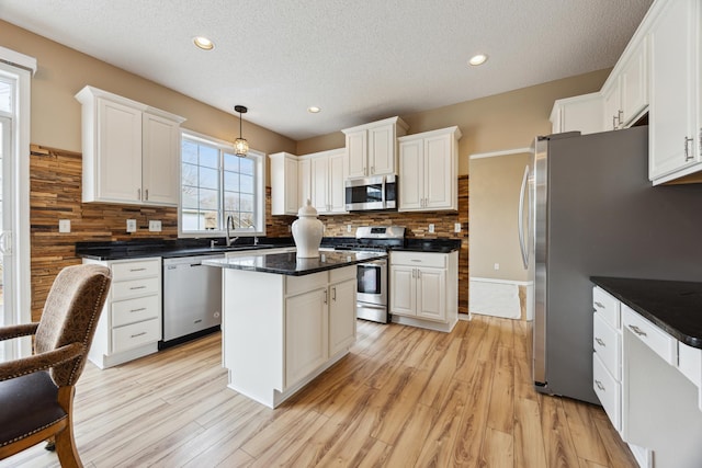 kitchen featuring a kitchen island, appliances with stainless steel finishes, decorative backsplash, light wood finished floors, and dark countertops