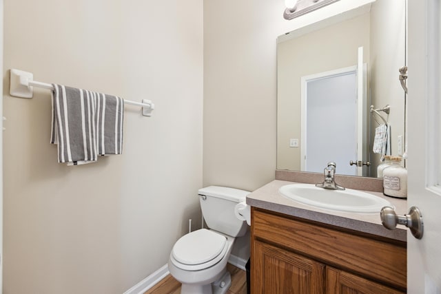 half bathroom featuring toilet, baseboards, and vanity