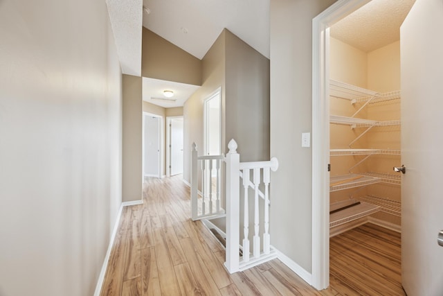 hallway featuring baseboards, wood finished floors, and an upstairs landing