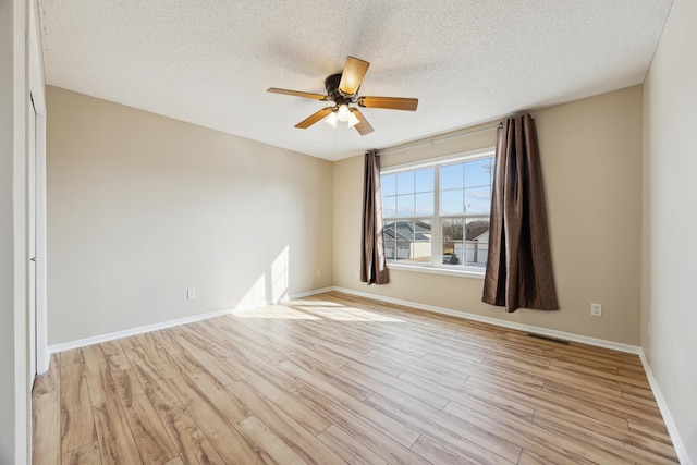 spare room featuring visible vents, light wood-style floors, ceiling fan, a textured ceiling, and baseboards