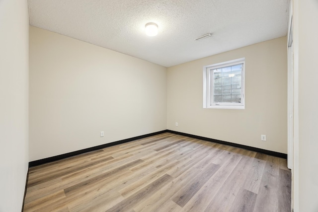 unfurnished room with light wood-type flooring, visible vents, a textured ceiling, and baseboards