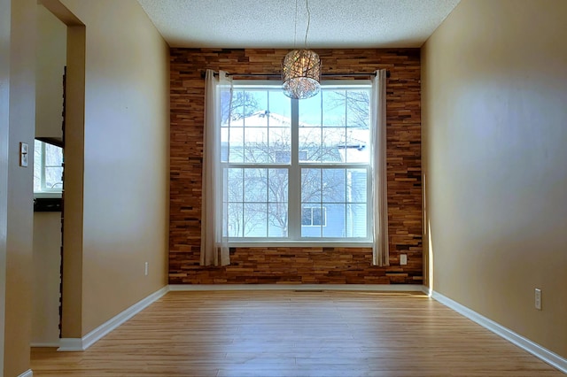 unfurnished dining area featuring a textured ceiling, wood walls, baseboards, and light wood-style floors