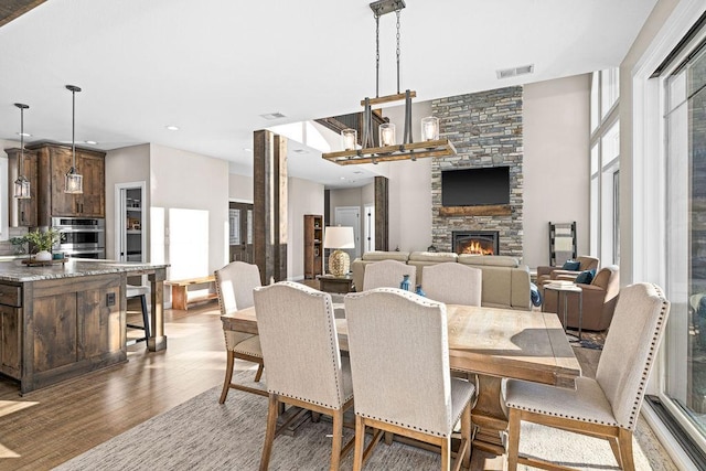 dining area featuring an inviting chandelier, wood-type flooring, and a stone fireplace