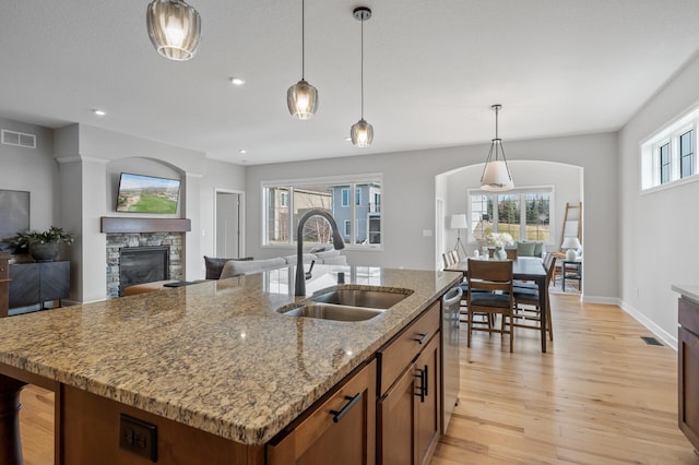 kitchen featuring sink, hanging light fixtures, light stone counters, a center island with sink, and a stone fireplace