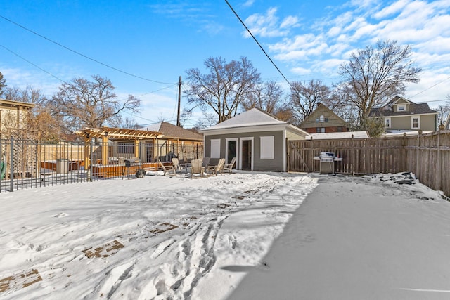 snow covered rear of property featuring a fenced backyard, a pergola, and an outdoor structure