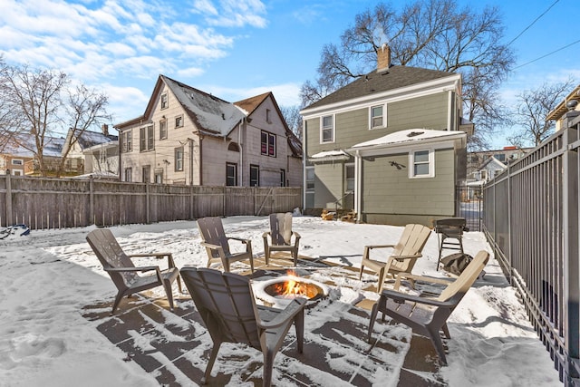 snow covered patio featuring a fire pit, an outdoor structure, a fenced backyard, and a residential view