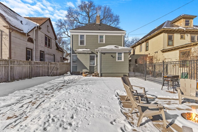 snow covered house featuring fence private yard, a fire pit, and an outdoor structure