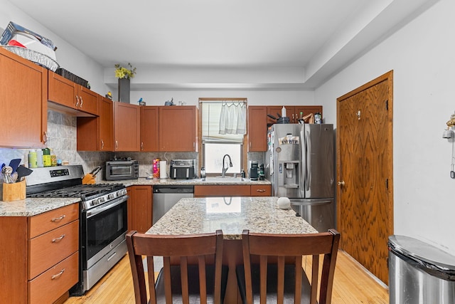 kitchen featuring tasteful backsplash, a kitchen island, appliances with stainless steel finishes, light stone counters, and a sink