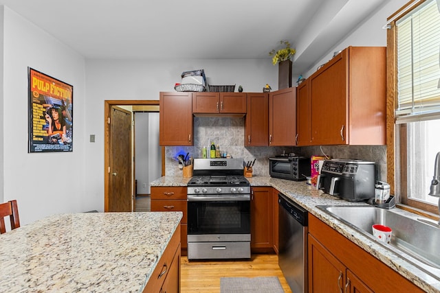 kitchen featuring stainless steel appliances, decorative backsplash, light wood-style floors, brown cabinetry, and a sink