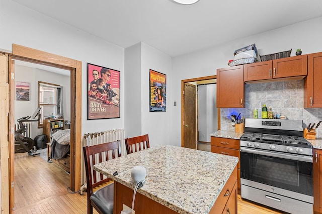 kitchen with tasteful backsplash, brown cabinetry, stainless steel range with gas stovetop, a kitchen island, and light stone countertops