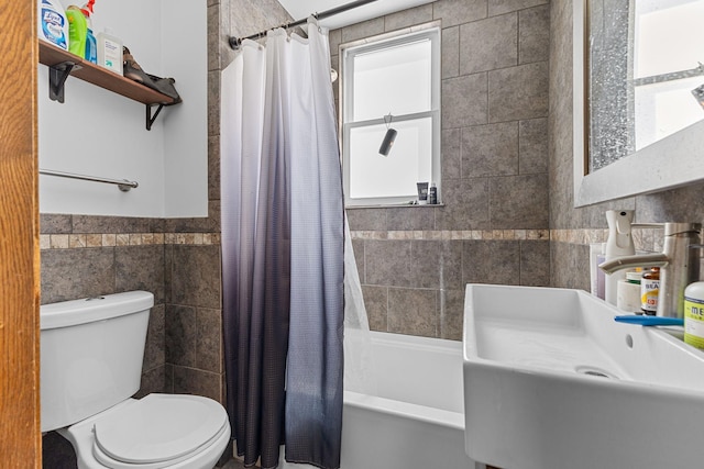 bathroom featuring toilet, tile walls, shower / bath combo with shower curtain, and a sink