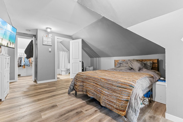 bedroom with lofted ceiling, light wood-style flooring, a spacious closet, ensuite bathroom, and baseboards