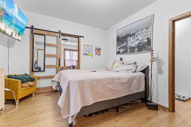 bedroom with light wood-style floors, a barn door, and baseboards